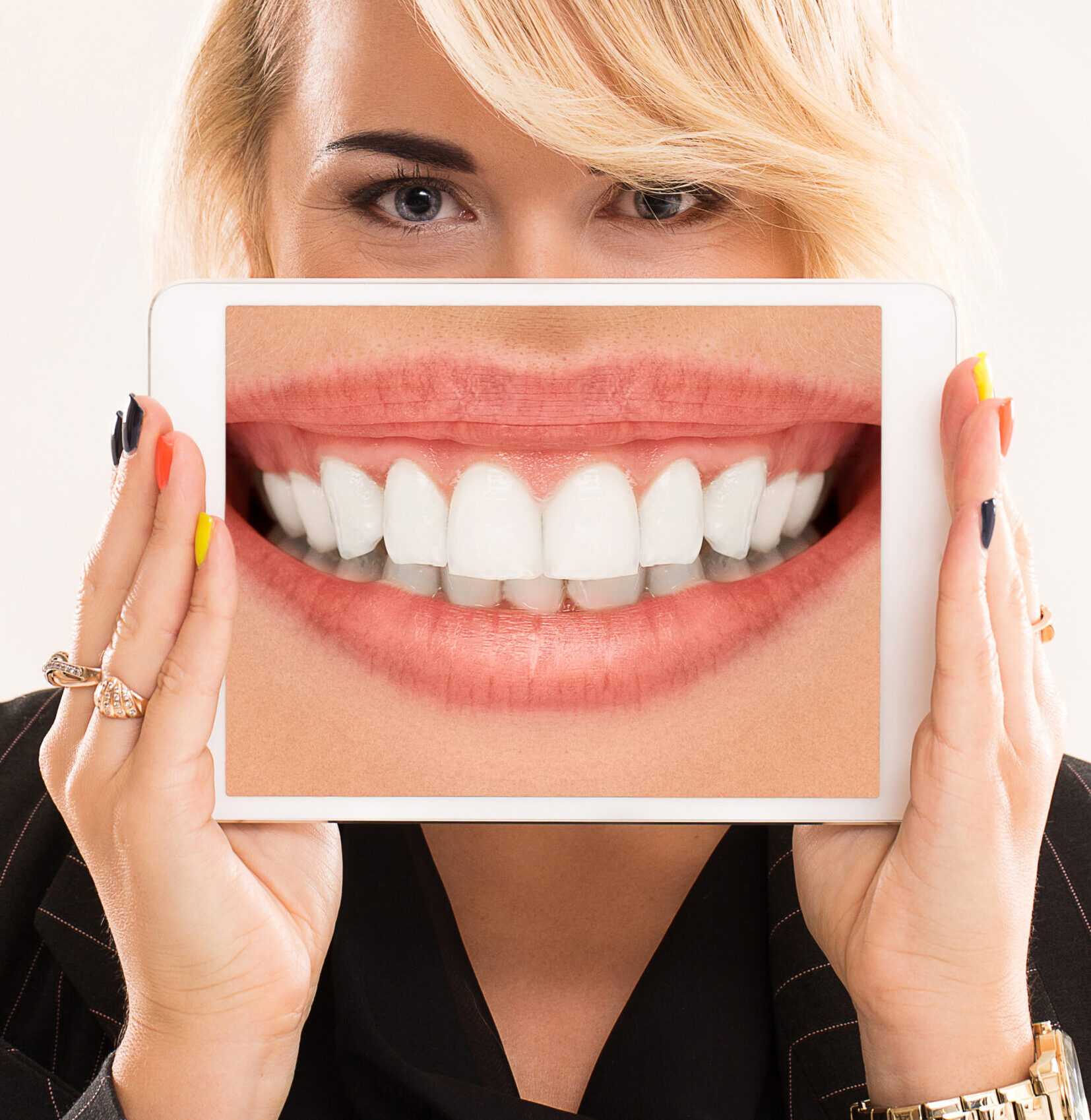 Beautiful woman with blonde hair and black suit is holding a tablet with large teeth on a screen